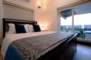 Stylish and comfortable bedroom at Kappad Beach House by Kisah Stays, featuring a cozy bed, elegant decor, and warm lighting. Designed for relaxation, this serene space offers a peaceful retreat with a luxurious ambiance, perfect for a restful stay by the beach in Kozhikode, Kerala.