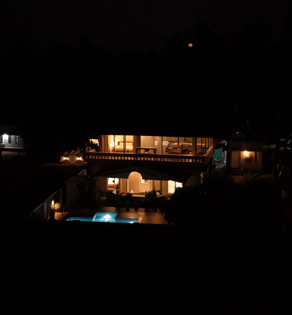 Nighttime view of Kappad Beach House by Kisah Stays, a oceanfront villa in Kozhikode, Kerala. The image showcases a beautifully lit private pool reflecting the ambient glow of the villa, surrounded by lush greenery and overlooking the serene Arabian Sea. The elegant architecture and outdoor seating create a perfect setting for a peaceful and scenic coastal retreat.