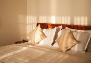 Warm sunlight streaming through the windows, gently illuminating the cozy bed in the bedroom of Kappad Beach House by Kisah Stays. The soft glow enhances the serene and inviting ambiance, creating the perfect setting for a relaxing beachfront retreat in Kozhikode, Kerala.
