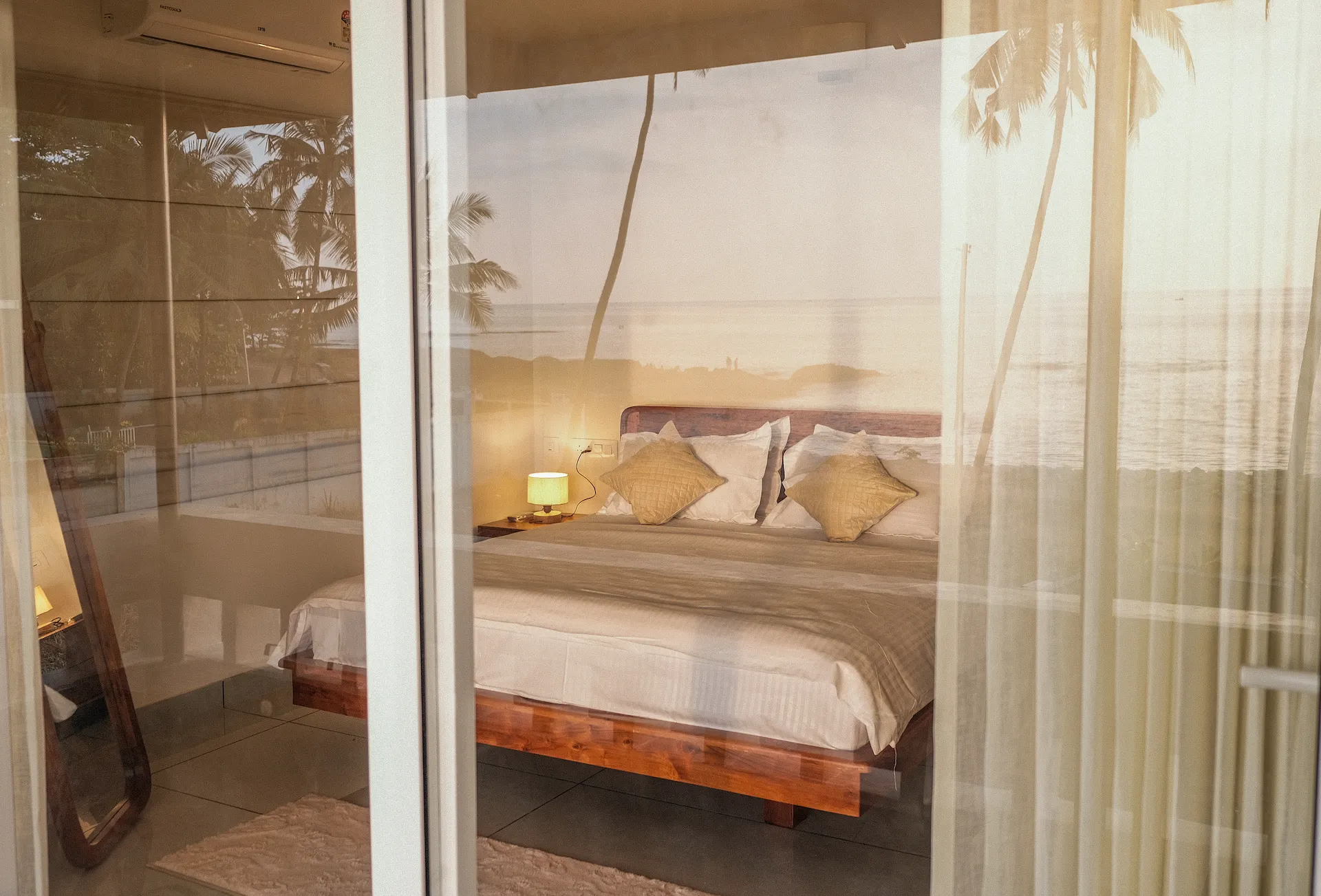 A captivating view of the room at Kappad Beach House by Kisah Stays, taken from outside the window. The glass reflects the stunning beach and Arabian Sea, blending the cozy interior with the breathtaking coastal scenery, creating a perfect harmony of luxury and nature in Kozhikode, Kerala