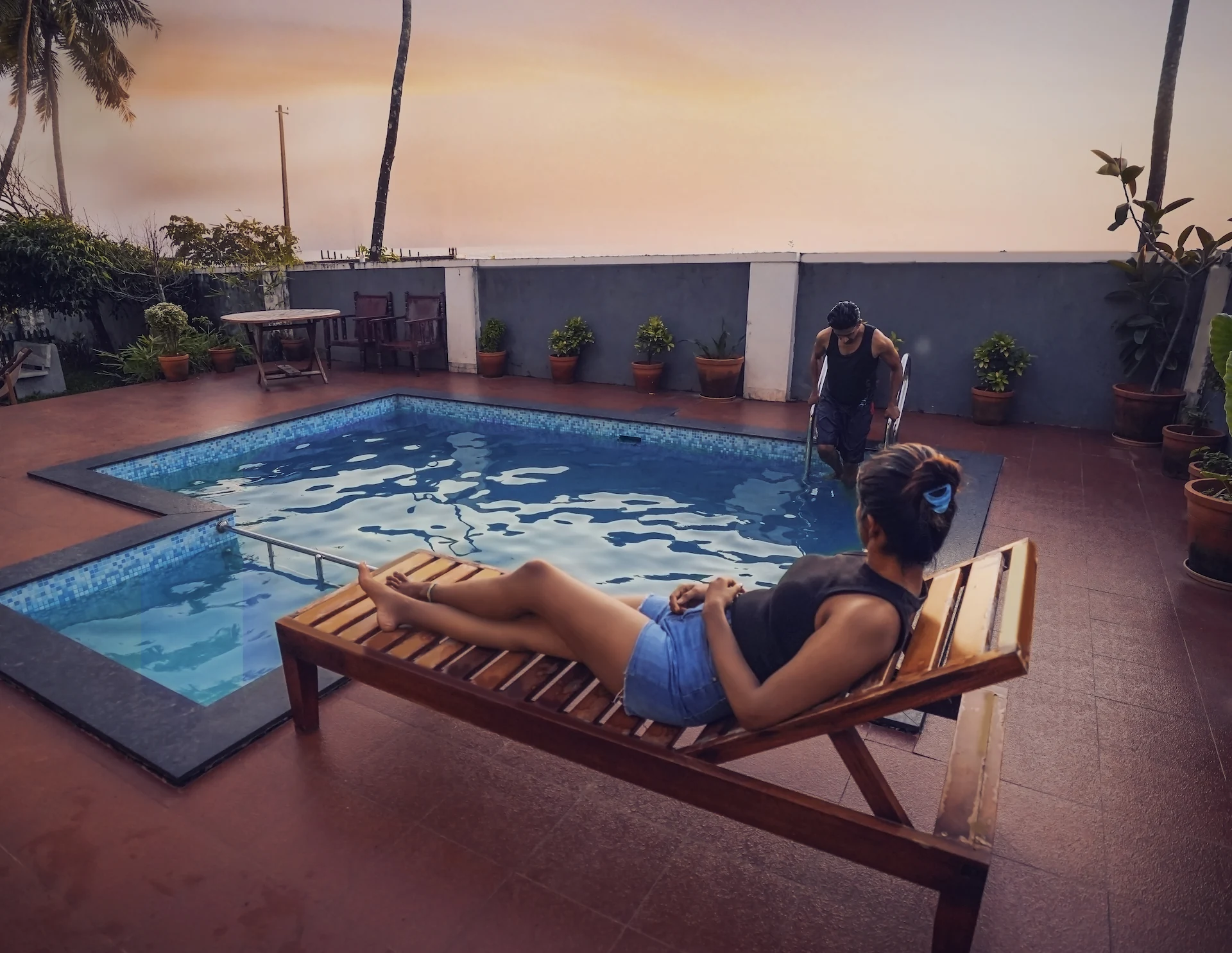 Two people, one girl sitting in the beach deck near the pool of Kappad beach in which another person is getting down to the pool. The view outside is just breathtaking.